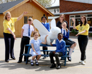 Pupils from Newlands Spring school sit around a picnic table on which is placed a large white bee sculpture